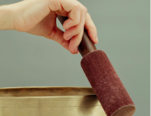 A hand tapping a meditational singing bowl.